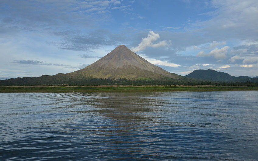 The imposing Arenal volcano and part of the Arenal lake subtly portrayed during a calm morning.